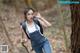 A woman in overalls and a backpack standing in the woods.