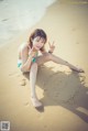 A woman sitting on the beach with a smiley face drawn in the sand.