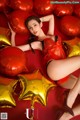 A woman laying on top of a pile of red and gold balloons.