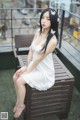 A woman in a white dress sitting on a wooden bench.