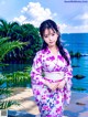 A woman in a kimono standing on a beach next to the ocean.