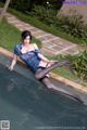 A woman in a blue dress and black stockings sitting on the edge of a pool.