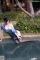 A woman in a blue dress and black stockings sitting on the edge of a pool.