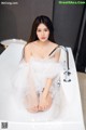 A woman sitting in a bathtub in a white dress.