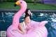 A woman in a white bikini sitting on a pink flamingo float.