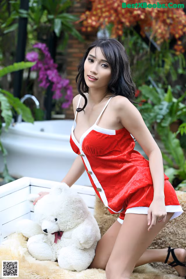 A woman in a red dress sitting next to a white teddy bear.