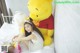 A woman sitting on a bed next to a large Winnie the Pooh stuffed animal.