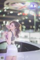 A woman standing next to a white car in a showroom.