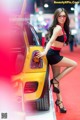 A woman standing next to a yellow car on a red carpet.