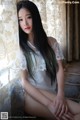 A woman with long black hair sitting on a window sill.