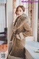 a woman standing in front of a window wearing a coat