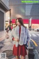 A woman in a red dress and a fur coat is walking down the street.