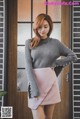 a woman in a gray sweater and pink skirt posing for a picture