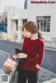 A woman in a red sweater is holding a brown bag.