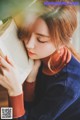 A woman is reading a book with her eyes closed.