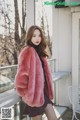 a woman in a pink fur coat standing on a balcony