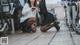 A couple of young women sitting next to each other on a sidewalk.