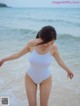 A woman in a white bathing suit standing on the beach.