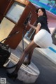 A woman in a white skirt and black stockings is filling up a gas pump.