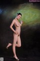 A nude woman in high heels posing in front of a painting.