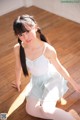 A young woman sitting on the floor in a white dress.