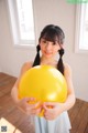 A young girl holding a yellow balloon in her hands.