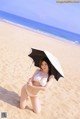 A woman in a white bikini holding an umbrella on the beach.