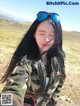 A woman in a camouflage jacket and sunglasses taking a selfie.