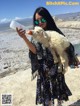 A woman holding a small white goat drinking water from a bottle.