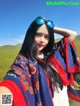 A woman wearing sunglasses and a colorful shawl in a field.