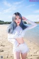 A woman with blue hair standing on a beach.