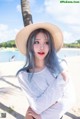 A woman with blue hair wearing a straw hat on the beach.