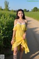 A woman in a yellow dress standing on a dirt road.