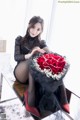 A woman sitting on a table holding a bouquet of red roses.