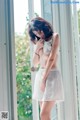 A woman in a white dress standing by a window.