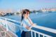 A woman in a school uniform leaning on a railing by the water.