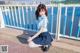 A woman in a blue shirt and skirt sitting on a railing.