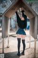 A woman in a skirt and stockings leaning against a wooden structure.