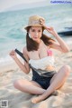 A woman sitting on the beach wearing a hat and overalls.