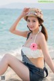 A woman in a bikini and hat sitting on the beach.