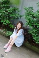 A woman sitting on the ground in front of a bush.