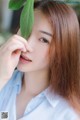 A woman holding a green leaf in front of her face.