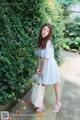 A woman in a blue and white striped dress holding a white bag.