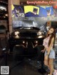 A woman standing in front of a batmobile at night.