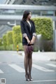 A woman in a black blazer and polka dot tights is standing on the street.