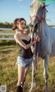 A woman standing next to a white horse in a field.