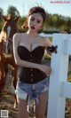 A woman standing next to a white fence with a horse in the background.