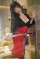 A woman in a red dress leaning against a glass door.