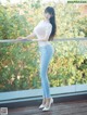 A woman in a white top and blue jeans posing on a balcony.