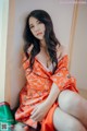 A woman in an orange kimono sitting on a window sill.